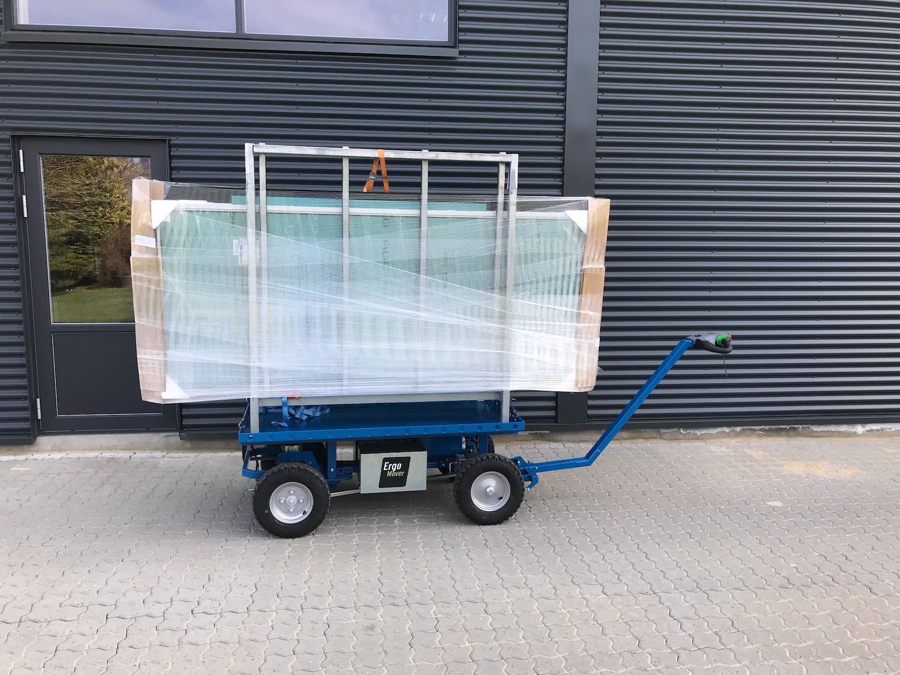 ErgoMover cart with a drawbar carrying packaged window units in a frame outside a dark cladded building.