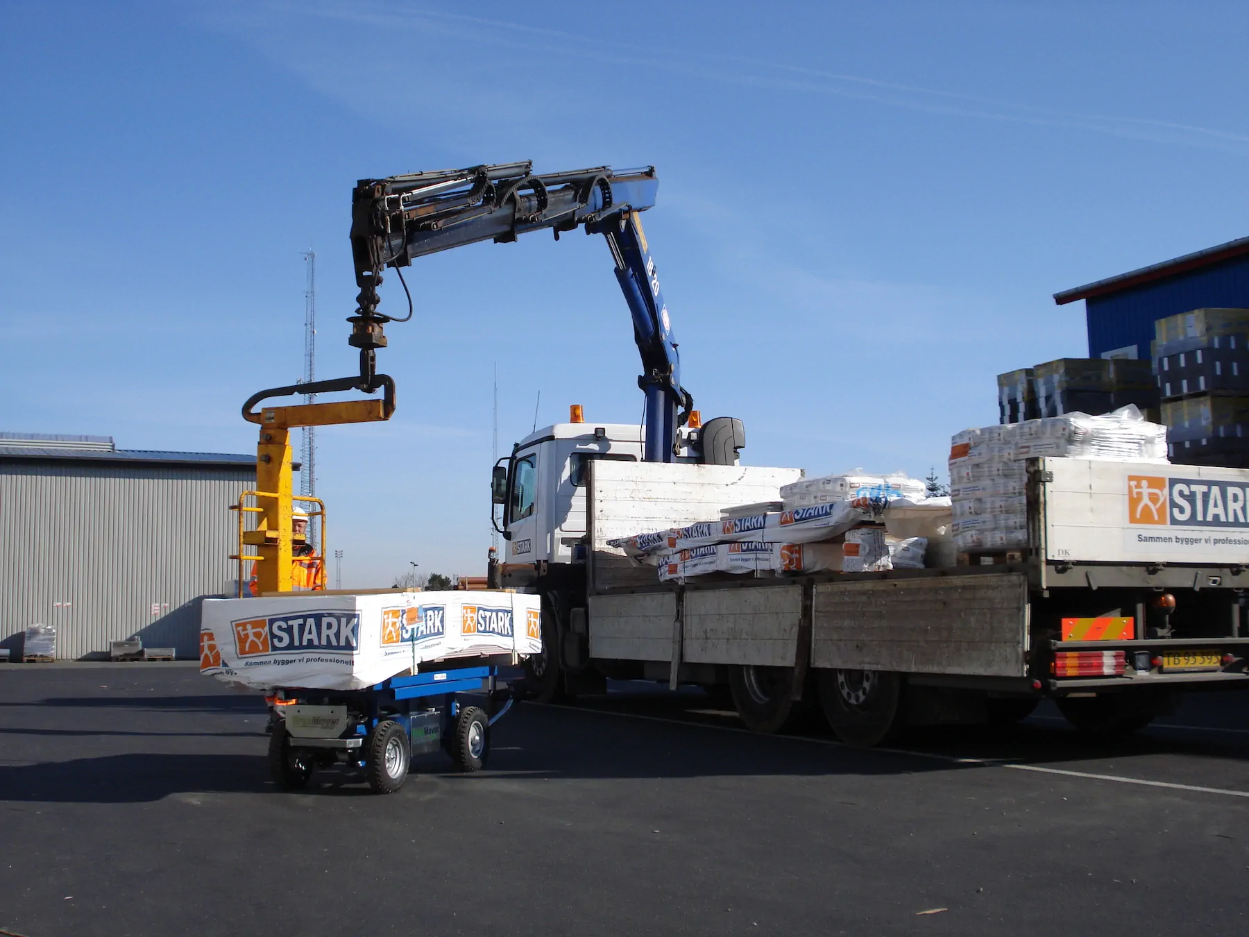 Truck-mounted crane lowering a wrapped pack onto a small ErgoMover cart next to a delivery truck.
