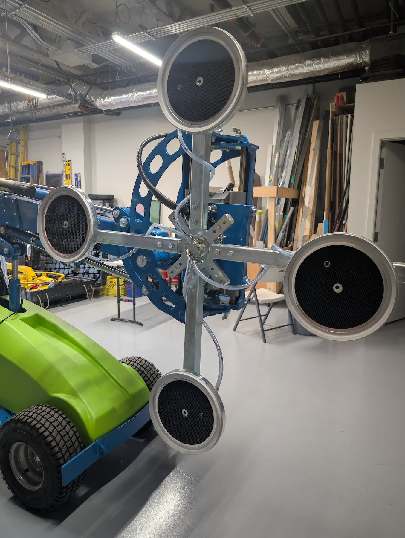 Close-up view of four circular vacuum suction cups connected by clear tubing to a cross-shaped metal bracket on the boom of a blue Winlet 600 robot.