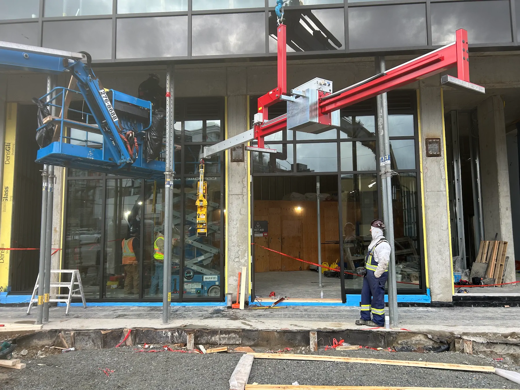 Counterbalance beam suspended from a crane in front of a ground-floor storefront, with its forward arm reaching into the glazing opening.