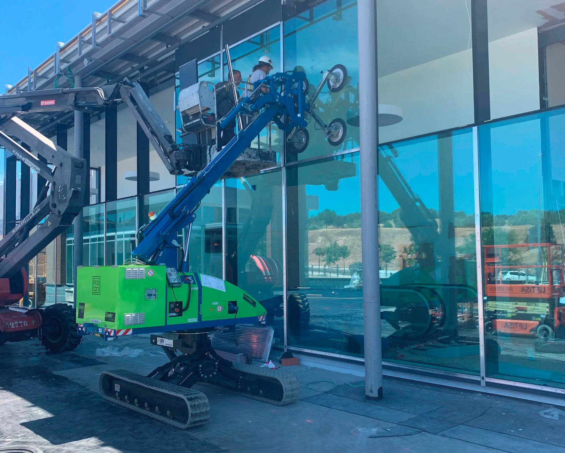 Winlet 1000 Crawler ER with its suction cups on a large glass unit at a glazed façade while a worker on an access platform guides the lift.